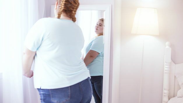 Bild adipöse Frau betrachtet sich im Spiegel